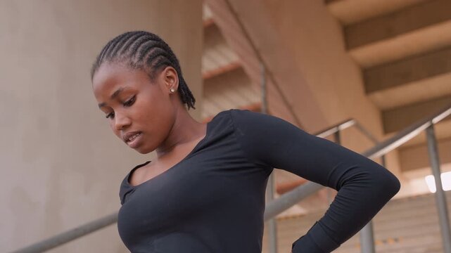 Black woman posing on concrete stairs. Hands on hip, confident gaze, cornrow braids, architectural railings, soft daylight, fashion attitude, contemplative mood, portrait study, poise and elegance.