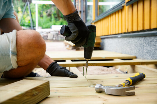 Homeowner using a power drill to install wooden deck planks during a backyard renovation, capturing realistic DIY, woodworking, outdoor construction.