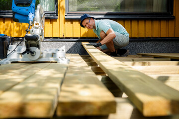 Man building wooden deck in backyard. Authentic DIY home improvement project during summer. Outdoor...