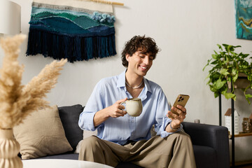 Obraz premium Stylish young man enjoying coffee while checking his phone in a chic modern apartment