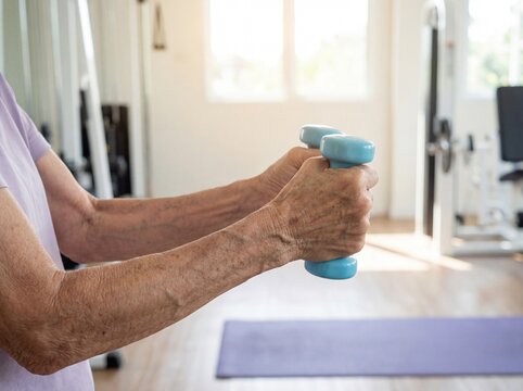 Sarcopenia (Muscle Loss): Professional photography, close-up of thin, frail elderly arms lifting a very small dumbbell, visible effort, bright morning gym setting.