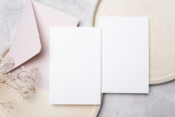 Fototapeta premium Blank wedding invitation card mockup featuring white cards and a pink envelope on a textured surface with dried flowers for elegant design presentation