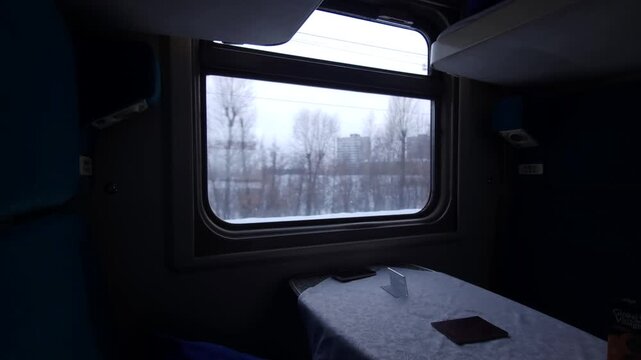Interior shot of a train compartment with a table, showing a snowy landscape outside the window, capturing the serene and intimate atmosphere of winter travel by train