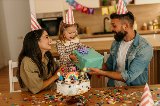 Young girl receiving gift from father with mother watching