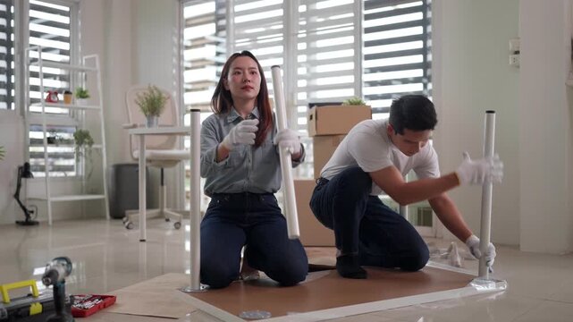 Asian couple adult assembling flat pack furniture together new home living room apartment interior home improvement project teamwork do it yourself happy moving in process