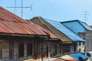 Obraz premium Different types of roofing materials on old traditional wooden houses. Residential house with mixed corrugated roofing sheets in different conditions. Various roofing materials in urban neighborhood