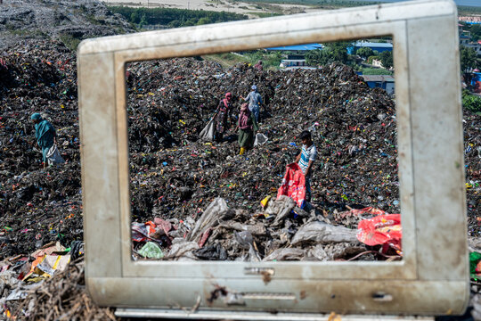 Chattogram, Bangladesh - 25 November 2025: View of figures amidst a vast, textured landscape of discarded waste, framed by an obsolete television set.