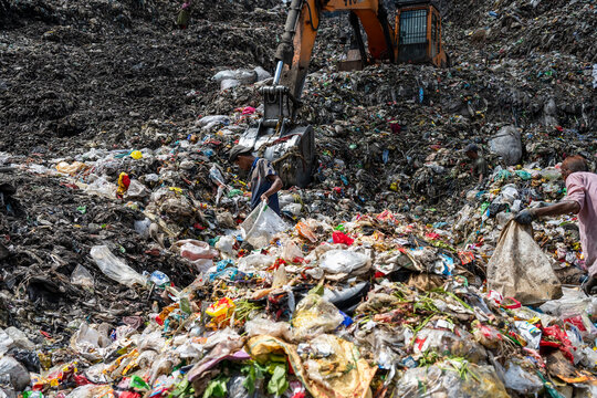 Chattogram, Bangladesh - 15 August 2025: View of a vast, chaotic landscape of discarded waste, where an excavator looms over scavengers amidst the sprawling landfill.