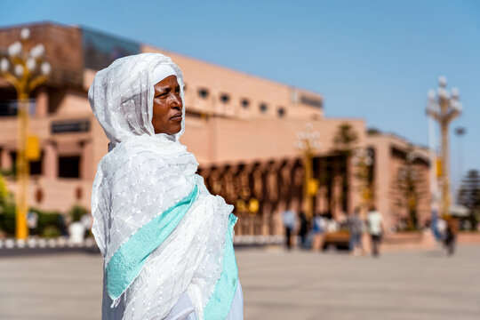 A woman dressed in a traditional white Habesha kemis and a matching netela shawl stands before the modern, tiered architecture of the Adwa Victory Memorial Museum in Addis Ababa.