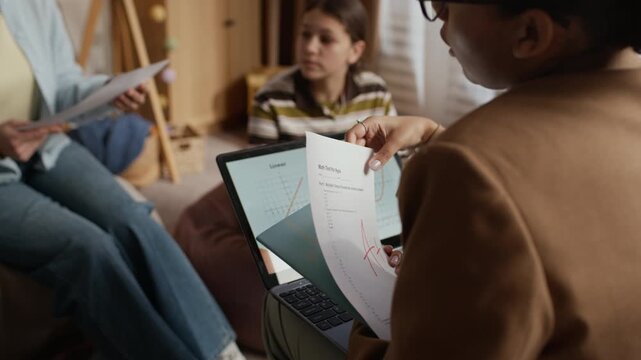 Female tutor giving last tests to mother who breaking into smile and looking at papers while communicating with tutor
