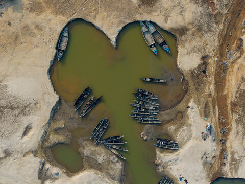 Aerial view of boats clustered in the heart-shaped water body, contrasting starkly with the parched earth surrounding it, Tahirpur, Sylhet Division, Bangladesh.