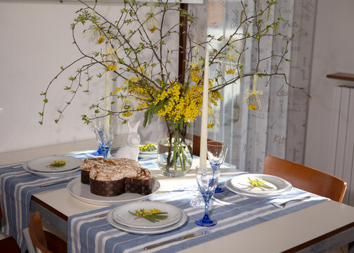 Dining table set for easter with traditional colomba pasquale, mimosa centerpiece, decorative eggs and white rabbit figurine, bright spring celebration ready scene