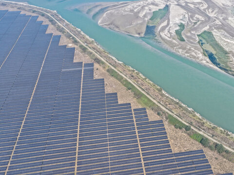Aerial view of rows of solar panels meet the winding river's edge, reflecting the sky's hue against the arid landscape, Gaibandha, Rangpur Division, Bangladesh.