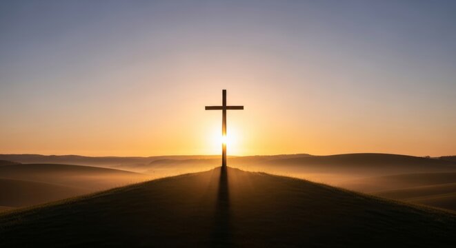 Silhouette of a simple wooden cross standing alone on a hill against a dramatic glowing bright yellow and orange sunrise sky for traditional christian happy easter religious resurrection concept.