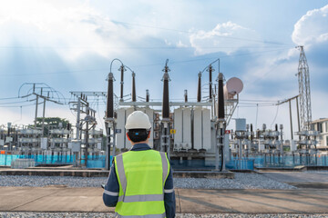 Obraz premium Engineer observing power transformer at electrical substation, assessing equipment condition and grid performance during routine inspection for energy reliability and operational safety.