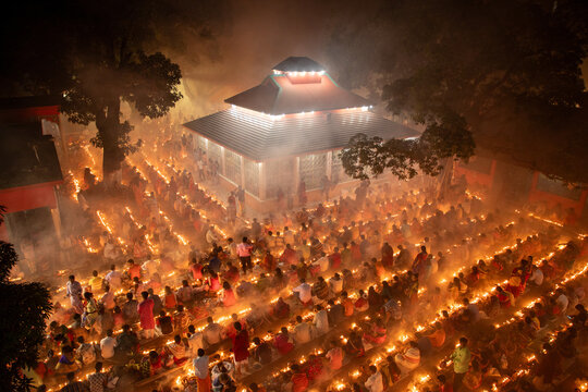 Aerial view of a temple bathed in golden light, surrounded by devotees holding flickering candles, a scene of serene devotion and vibrant illumination, Narayanganj, Bangladesh.