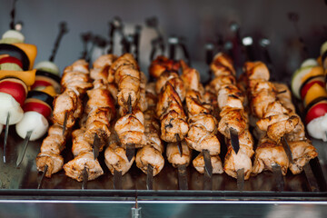 Grilled chicken, beef or pork meat skewers shish kebab shashlik cooking on a metal grill, surrounded by colorful vegetables like onions, peppers, and tomatoes.
