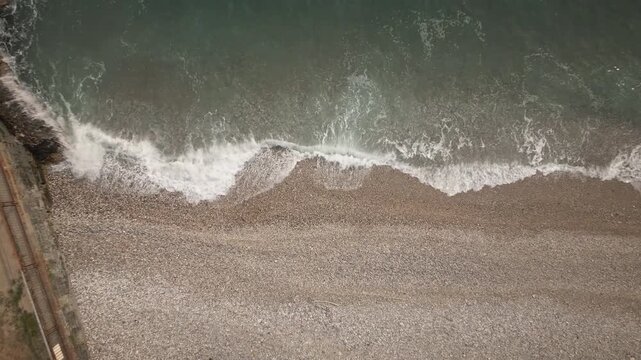 Loop-ready 4K UHD static overhead shot of foamy waves washing over a pebble beach shoreline; soothing natural texture for commercials, intros, wellness backgrounds.