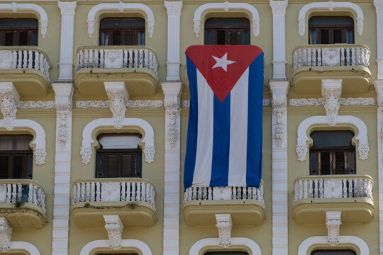 A large Cuban flag waving vertically from the balcony at the facade of an old colonial building. Havana, Cuba.	
