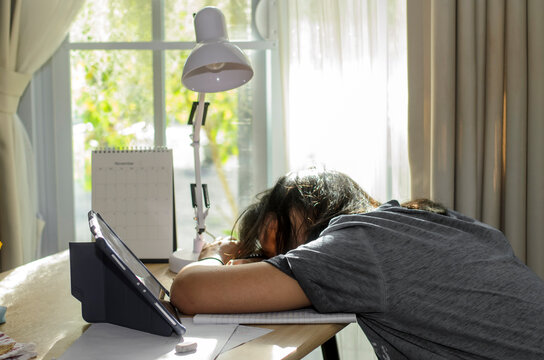 Tired Asian Students study online to study for the exam. Children using tablet and laptop to learn and do homework at home, sleeping on desk after studying and doing homework. Education concept.