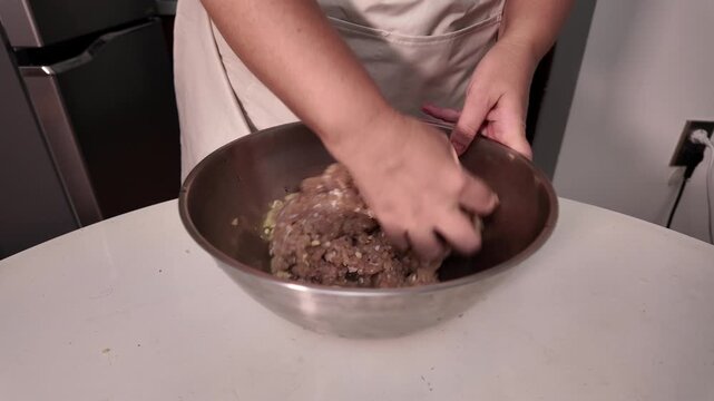 A woman mixes minced meat in a metal bowl, cooking homemade food