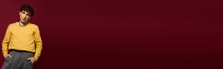 Stylish man showcases modern fashion against bold burgundy backdrop with confidence