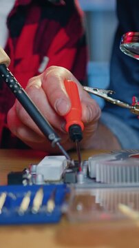 Unrecognizable skillful man and boy helping each other during repairing special panel with soldering iron, screwdriver and stand with magnifying glass on workplace