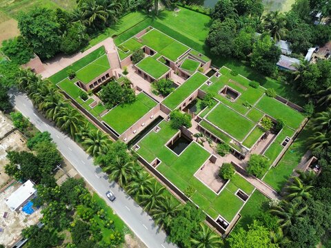 Gaibandha, Bangladesh - 21 June 2025: Aerial view of a building with lush green rooftops contrasting with the surrounding trees and a road with a car passing by.