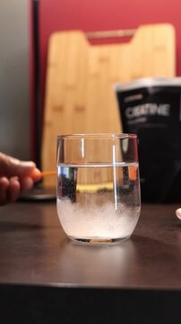 Person mixing creatine monohydrate nutritional supplement powder in glass of water with a spoon for muscle growth and performance