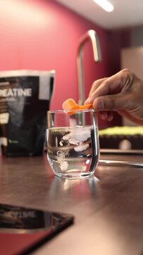 Person mixing creatine supplement powder into a glass of water for a pre workout sports drink in a modern kitchen