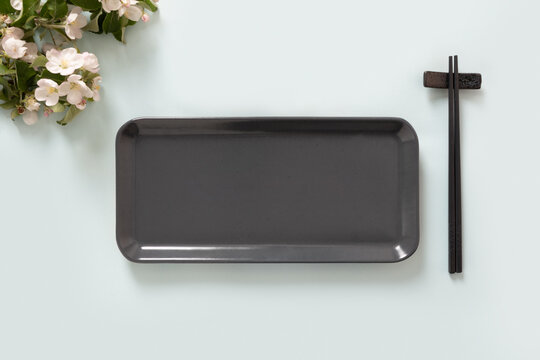 Minimal table composition with dark rectangular sushi plate and chopsticks on light background. Clean food styling with soft light and copy space.
