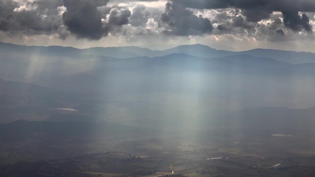 Panoramic view of sun rays breaking through mixed clouds above a vast flat plain in France geography. Golden beams illuminate broad lowlands while dynamic cloud patterns enhance the French landscape.