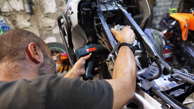 Professional mechanic repairing engine of motorcycle at workshop. Male repairer fixing motor of motorbike using tool at workplace. Adult repairman working at garage. Concept of maintenance service