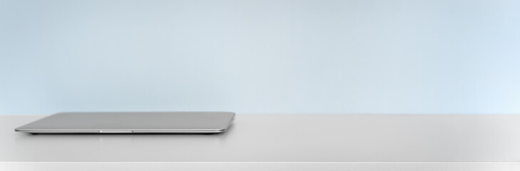 Closed laptop on white desk with blue wall background