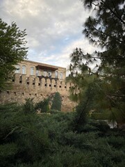 Fototapeta premium An elegant multi-story stone building featuring classic arched windows and balconies rises above lush Mediterranean landscaping