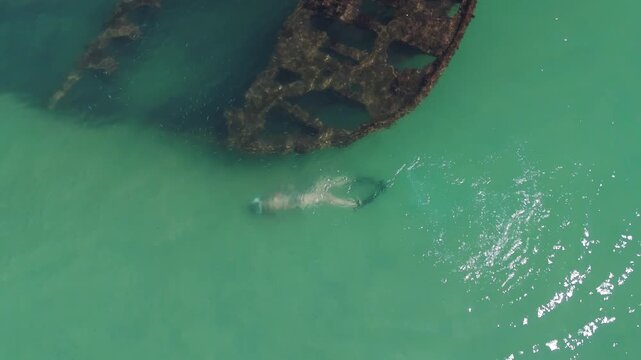 Snorkeling near the shipwreck, aerial footage. Aerial view of the shipwreck with woman swimming around it. Island of Santa Catarina near the city of Florianopolis.