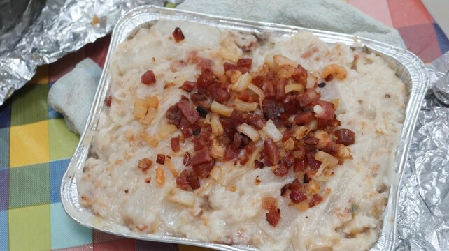 close up of Hong Kong traditional style homemade Chinese steamed turnip cake topped with Chinese sausage, dried shiitake mushrooms and dried shrimp in a Foil container on a white plate over colorful c
