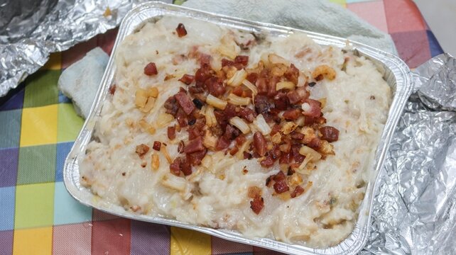 close up of Hong Kong traditional style homemade Chinese steamed turnip cake topped with Chinese sausage, dried shiitake mushrooms and dried shrimp in a Foil container on a white plate over colorful c