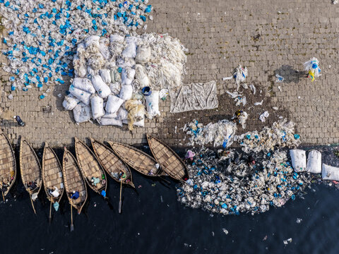Aerial view of boats moored near piles of discarded plastic waste on the banks of the Buriganga River, Dhaka, Dhaka Division, Bangladesh.