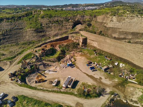 Aerial view of the old quarry revealing layers of earth and exposed rock faces with scattered machinery and construction equipment, Estepona, Andalusia, Spain.