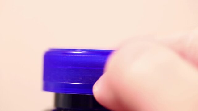 Macro close-up of a hand screwing on a blue plastic bottle cap.