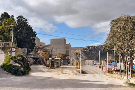 Manilva, Spain - 18 February 2026: View of the quarry entrance and weighbridges under a cloudy sky, its rough textures contrasting with the smooth road and surrounding greenery.