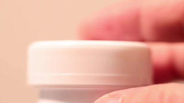 Macro close-up of a hand screwing a white lid onto a white plastic jar.