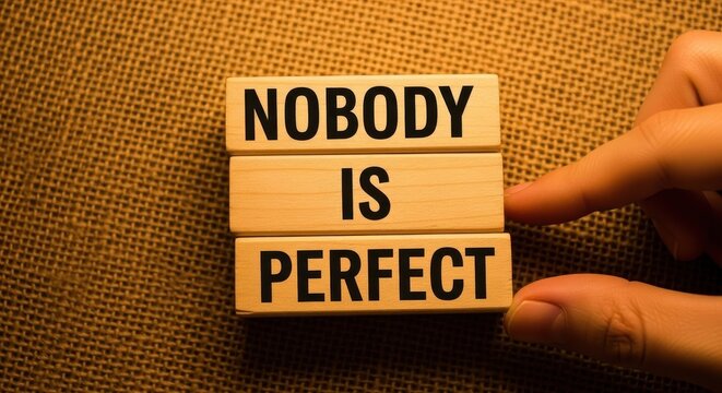 A hand pointing at wooden blocks spelling out 'nobody is perfect' against a fabric background