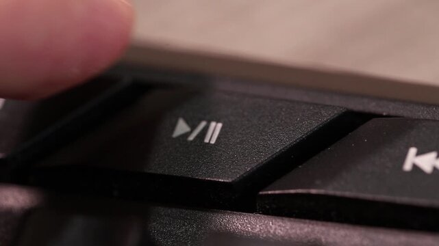 Pressing media control button to start or stop music and video, macro shot of human finger.