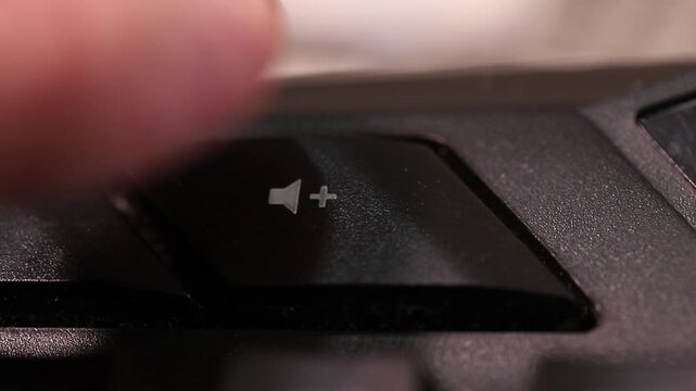 Increasing sound level on a computer keyboard, macro shot of human finger clicking the volume boost button.