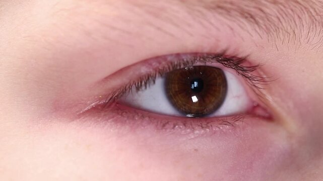 Extreme macro close-up of a young boy's brown eye looking into the distance and blinking calmly.