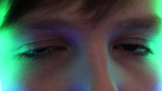 Extreme macro of a young boy's eyes reflecting colorful running neon lights in the dark