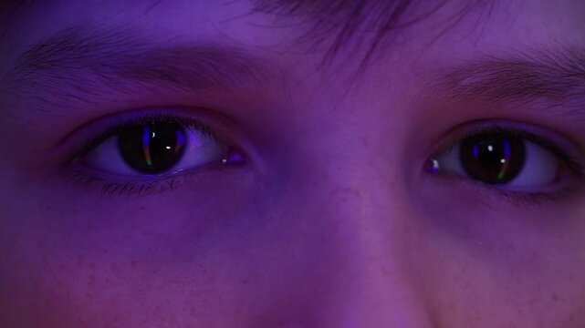 Extreme macro of a young boy's eyes reflecting colorful running neon lights in the dark