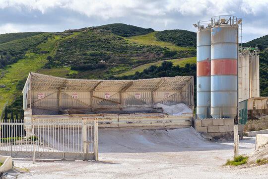 Manilva, Spain - 18 February 2026: View of an industrial concrete facility with aggregate bunkers and tall cylindrical tanks against a backdrop of rolling green hills.